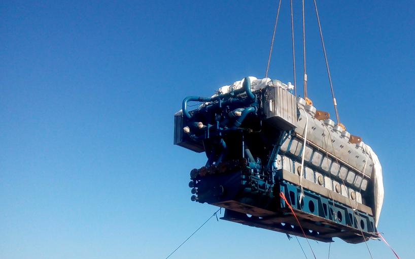Large engine lifted by crane against a blue sky